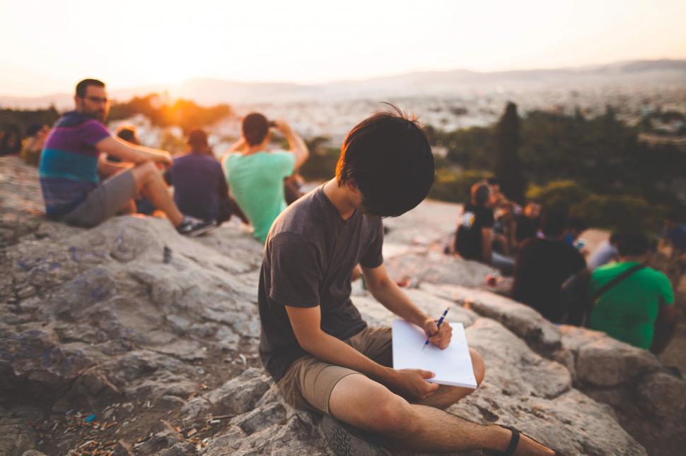Free Image of A man sitting on a rock with a pen in his hand 