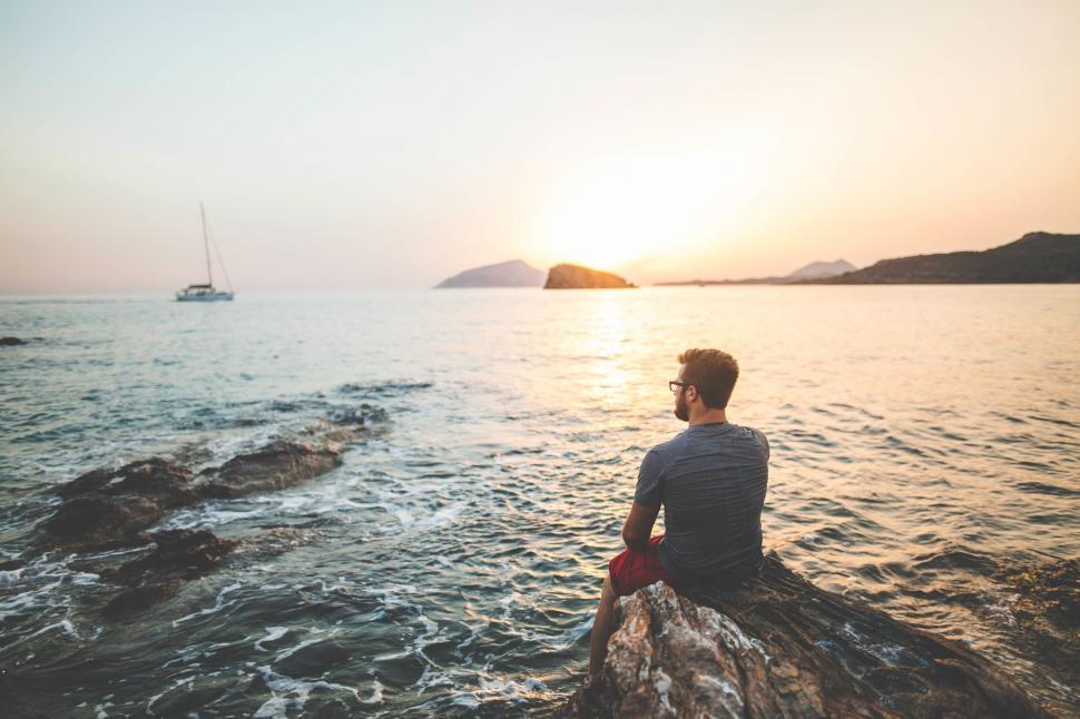 Free Image of A man sitting on a log looking at the ocean 
