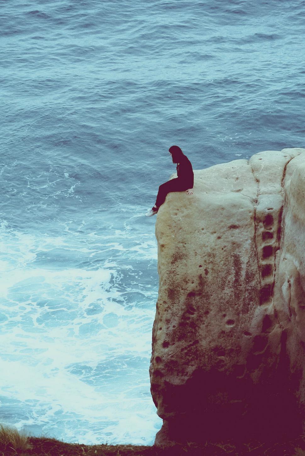 Free Image of A person sitting on a rock above the water 