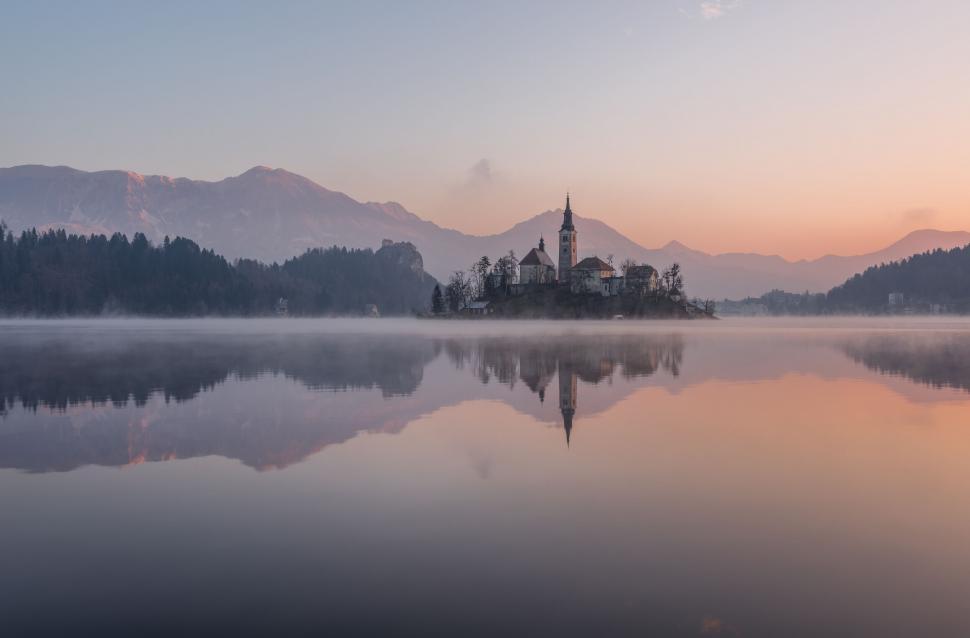 Free Image of A small island with a church on it and a body of water with mountains in the background 