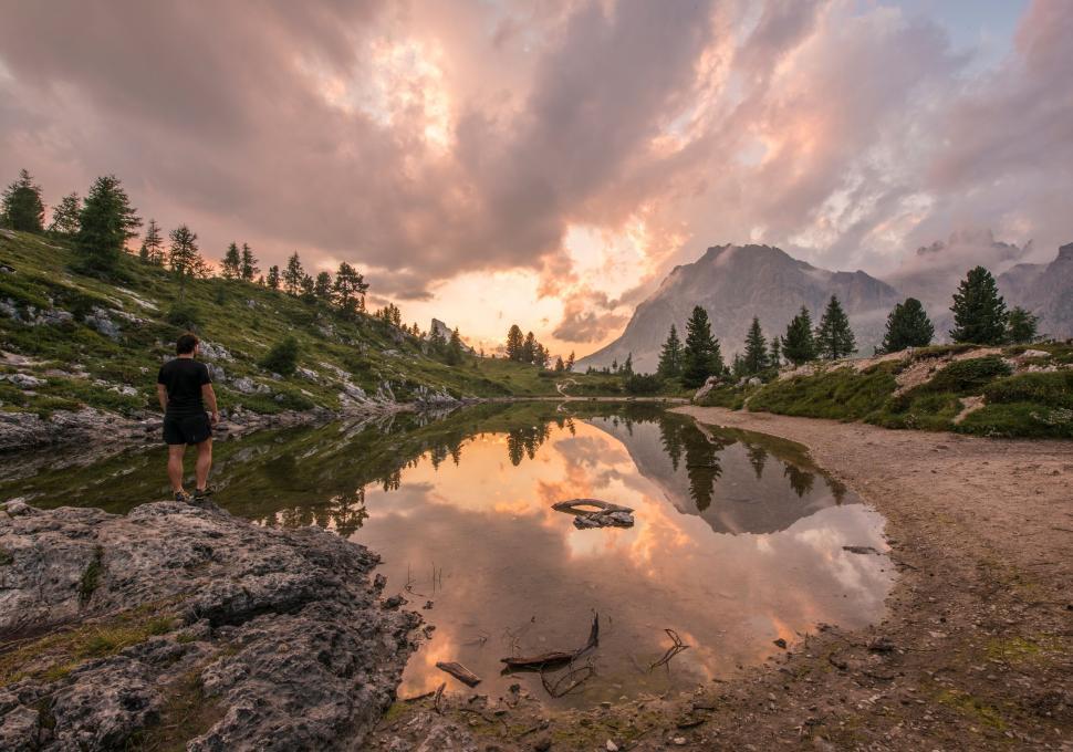 Free Image of A man standing on a rocky shore near a lake 
