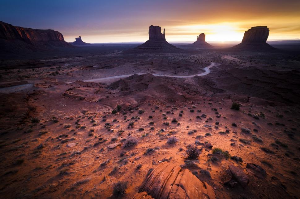 Free Image of A landscape of a desert with a dirt road and tall rock formations 
