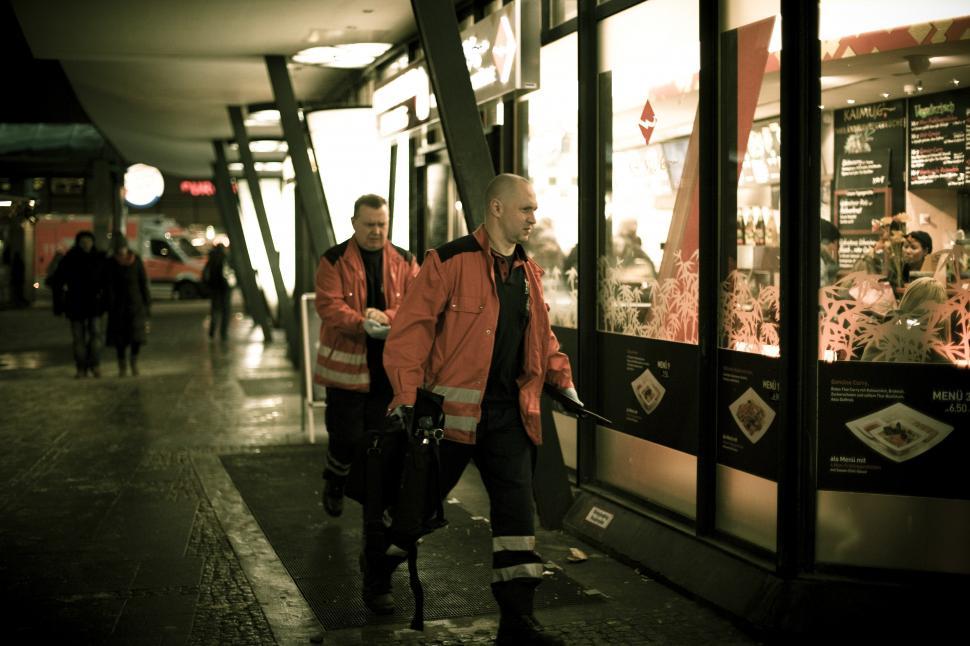 Free Image of A group of men in orange jackets walking down a sidewalk 