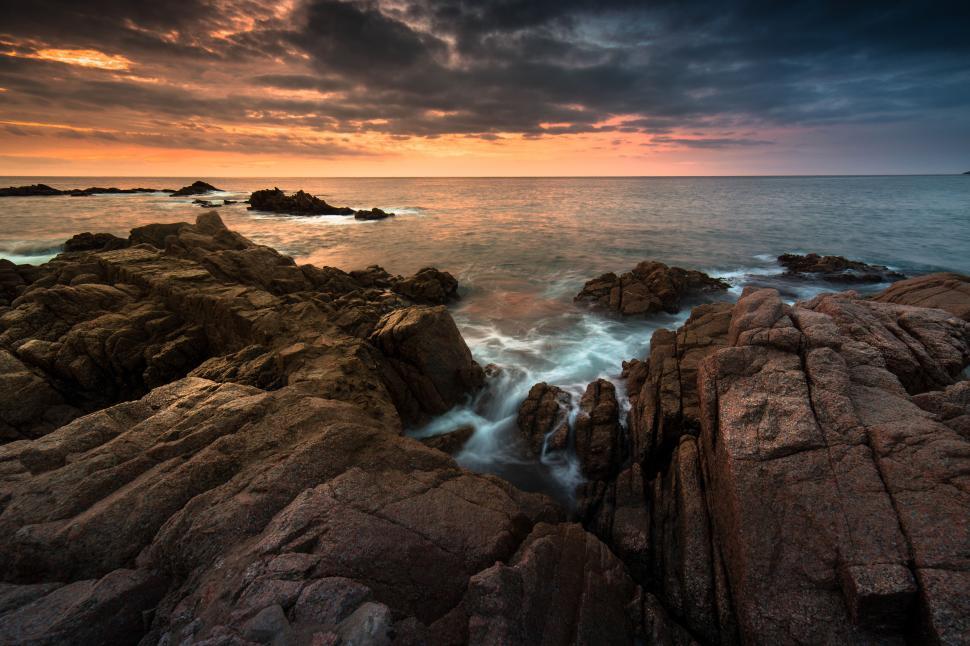 Free Image of A rocky beach with water and a sunset 