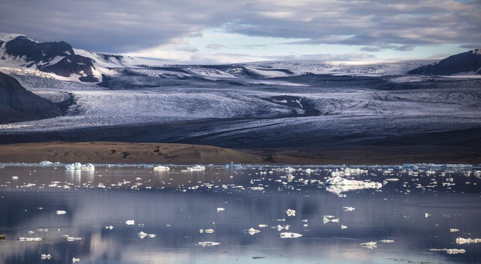 Free Image of Icebergs floating in a body of water with snow covered hills in the background 