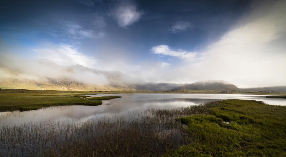 Free Image of A lake with grass and mountains in the background 