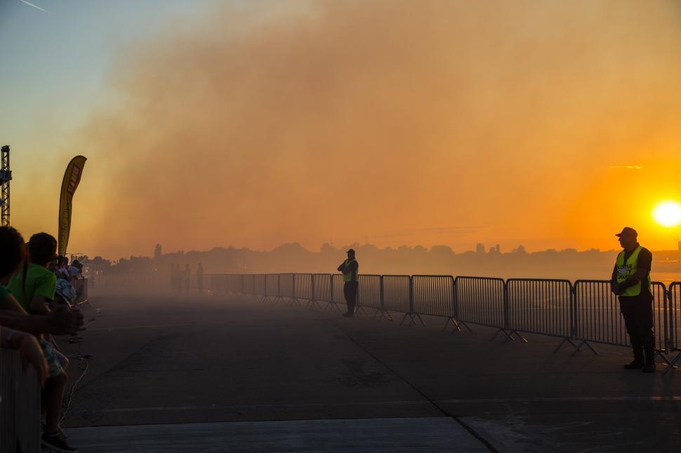 Free Image of A person standing on a sidewalk with a fence in front of a sunset 