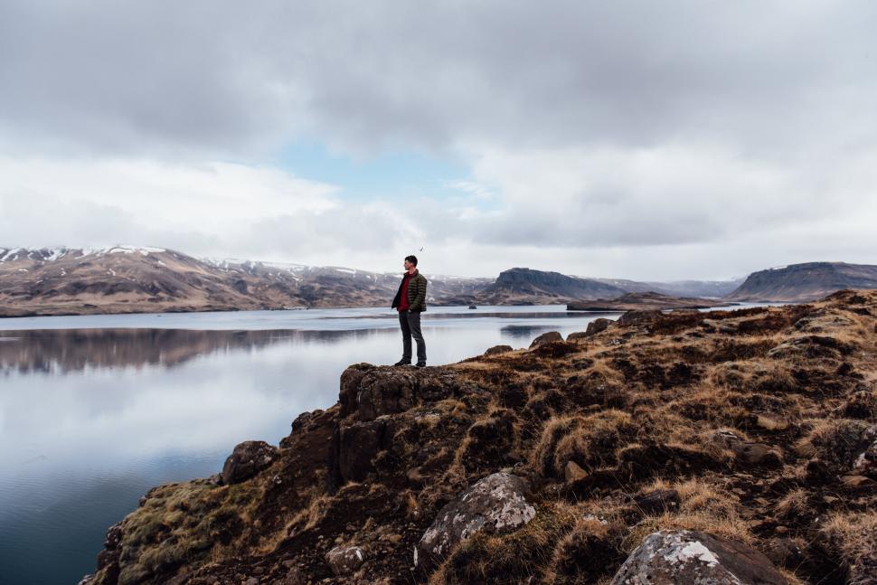 Free Image of A man standing on a rocky cliff overlooking a body of water 
