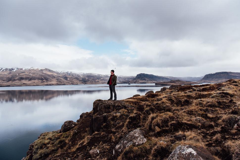 Free Image of A man standing on a rocky cliff overlooking a body of water 