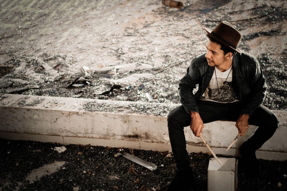 Free Image of A man sitting on a ledge with a stick 