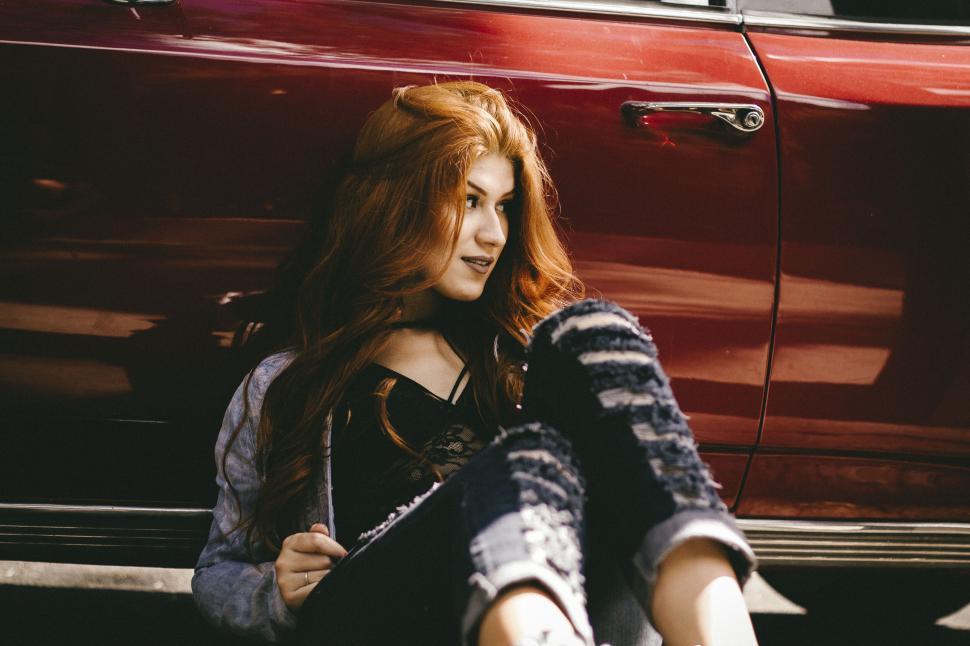 Free Image of A woman sitting in front of a red car 