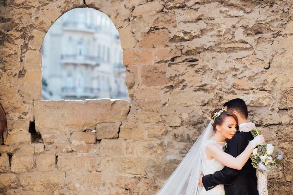 Free Image of A man and woman hugging in front of a stone wall 