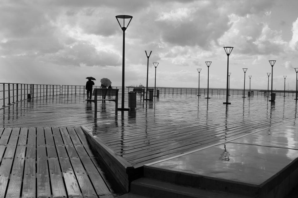 Free Image of People standing on a bench with umbrellas in the rain 