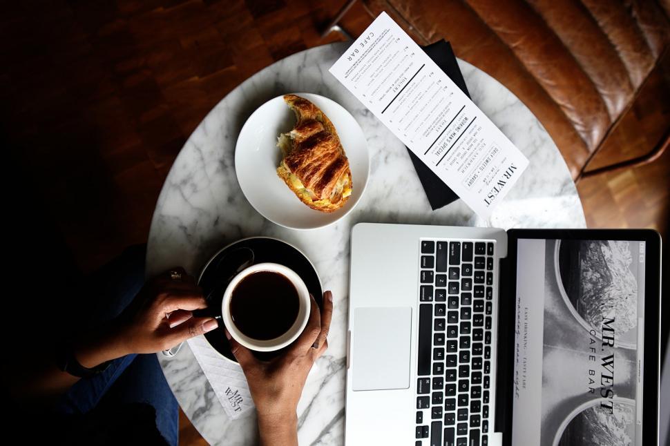 Free Image of A person holding a cup of coffee and a sandwich on a table 