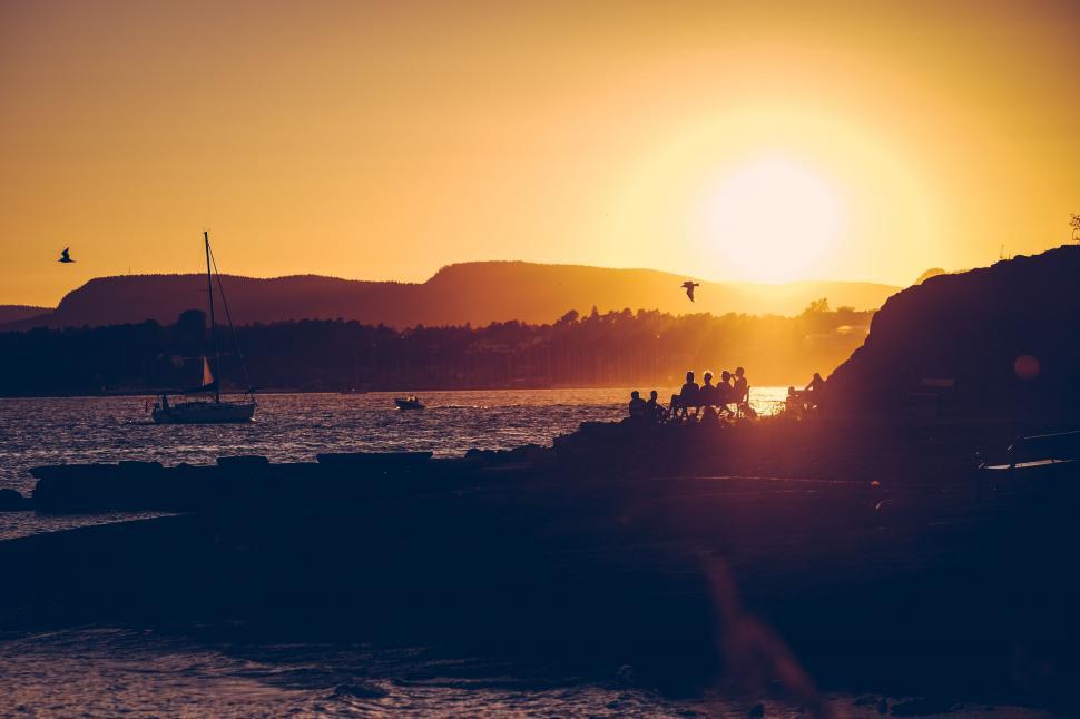 Free Image of A group of people sitting on a rock by the water with a sailboat 
