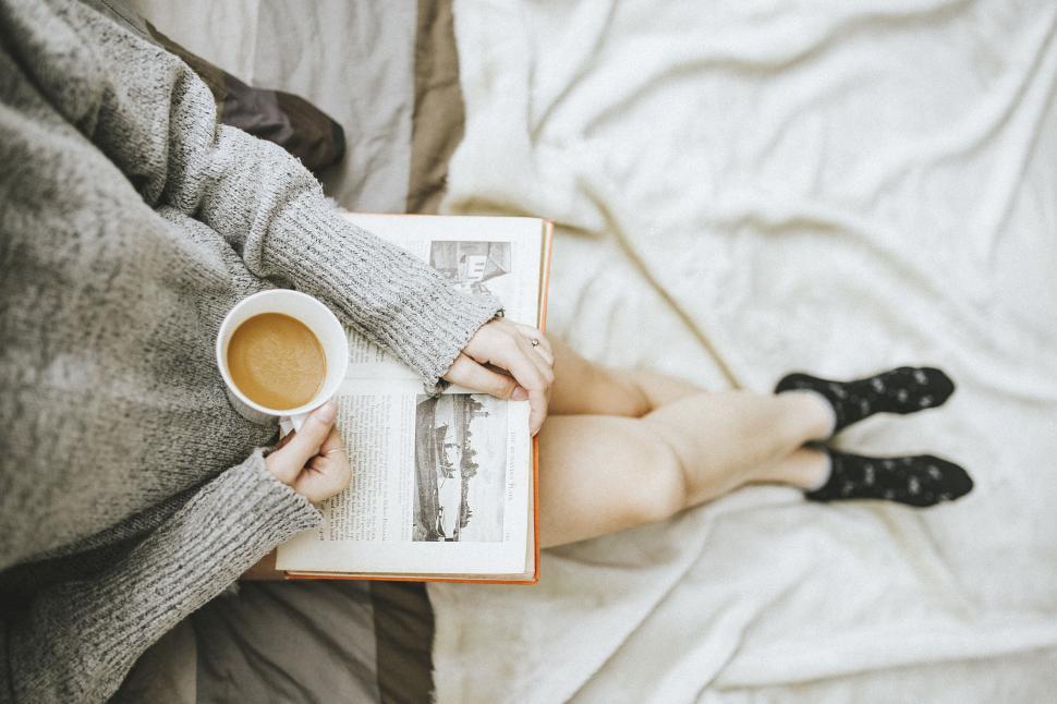 Free Image of A person holding a cup of coffee and a book 