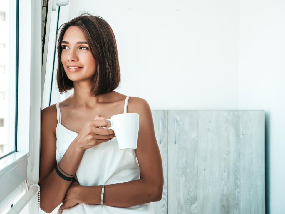 Free Image of A woman holding a cup looking out a window 