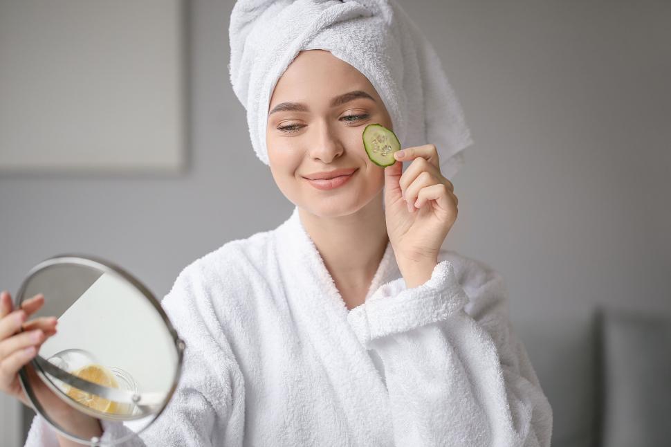 Free Image of A woman in a white robe holding a slice of cucumber 