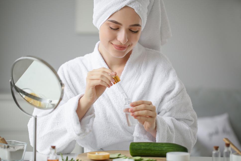 Free Image of A woman in a white robe holding a small bottle with a dropper 