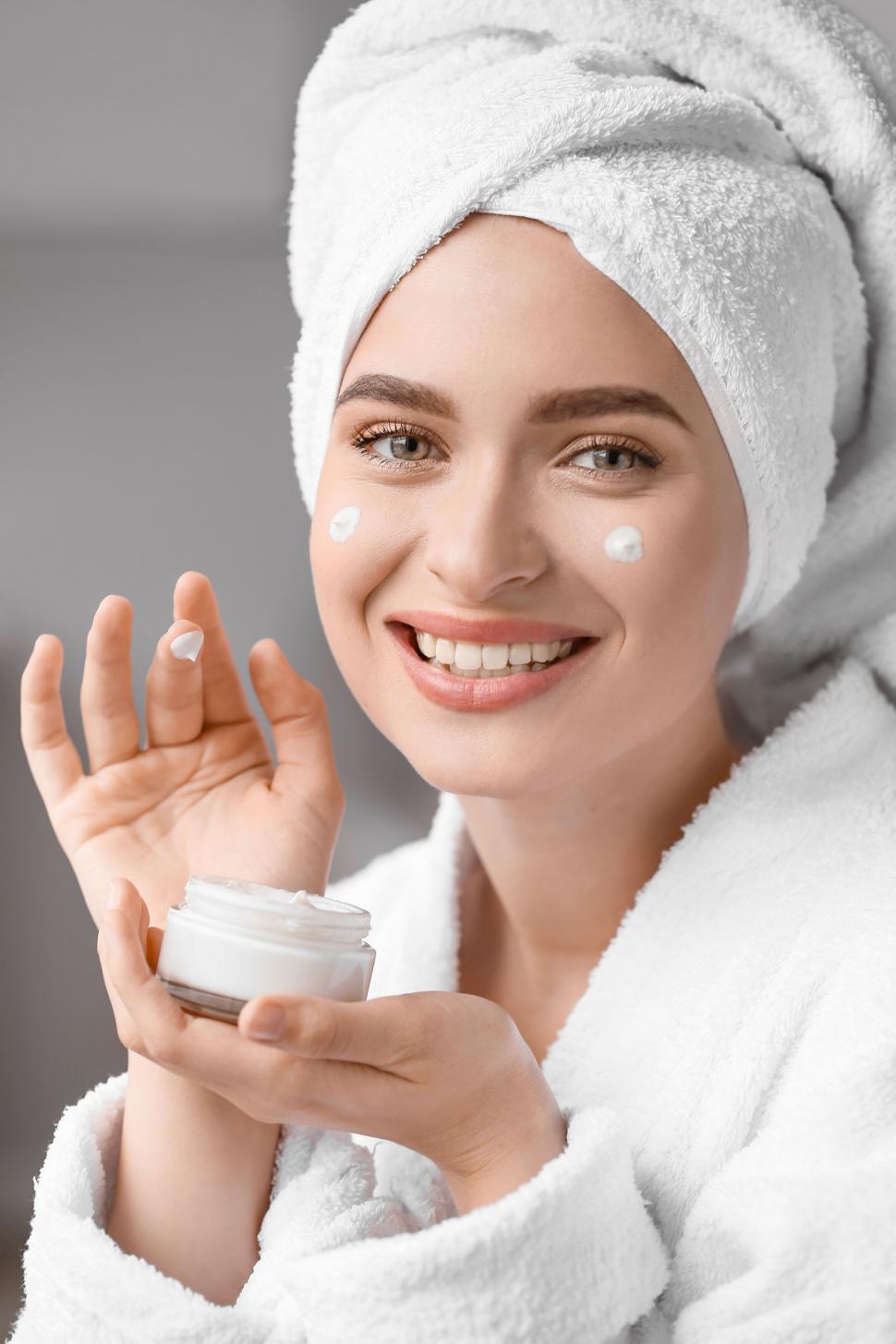 Free Image of A woman wearing a white robe and holding a jar of cream 