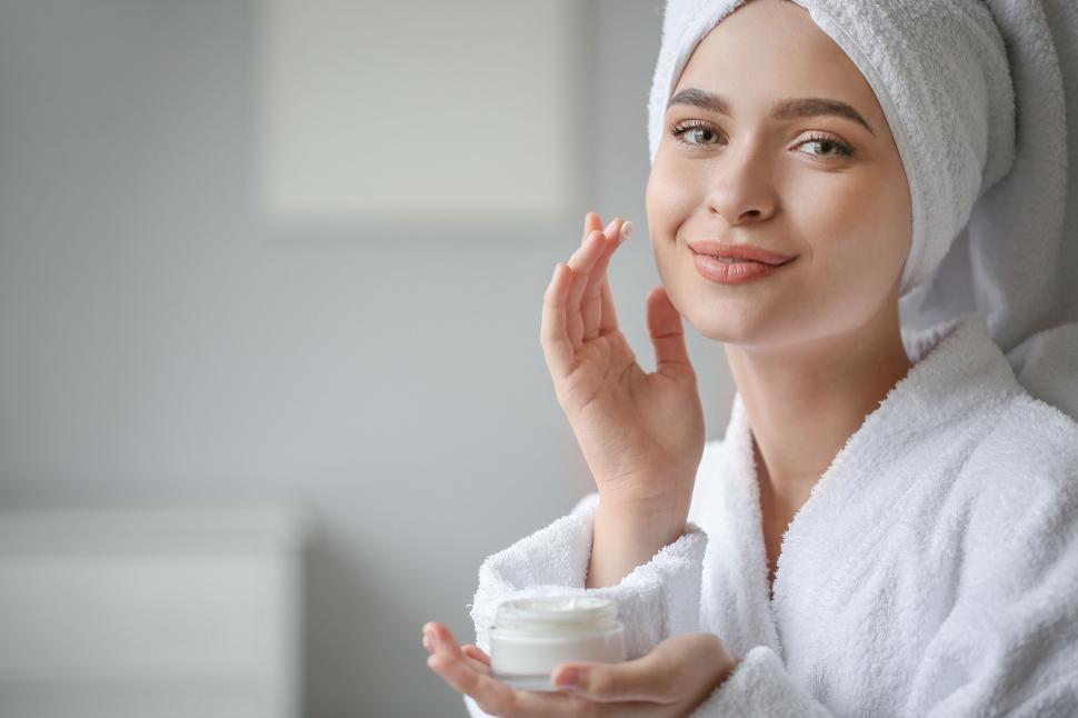 Free Image of A woman wearing a white robe and holding a cream jar 