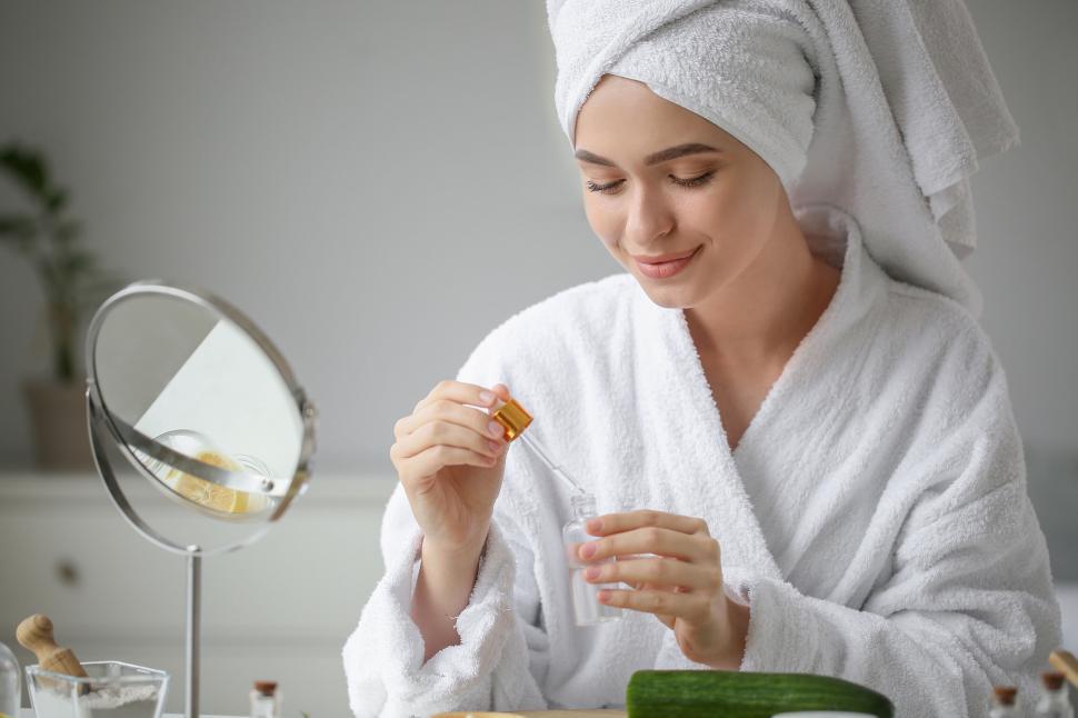 Free Image of A woman in a white robe holding a small bottle with a dropper 