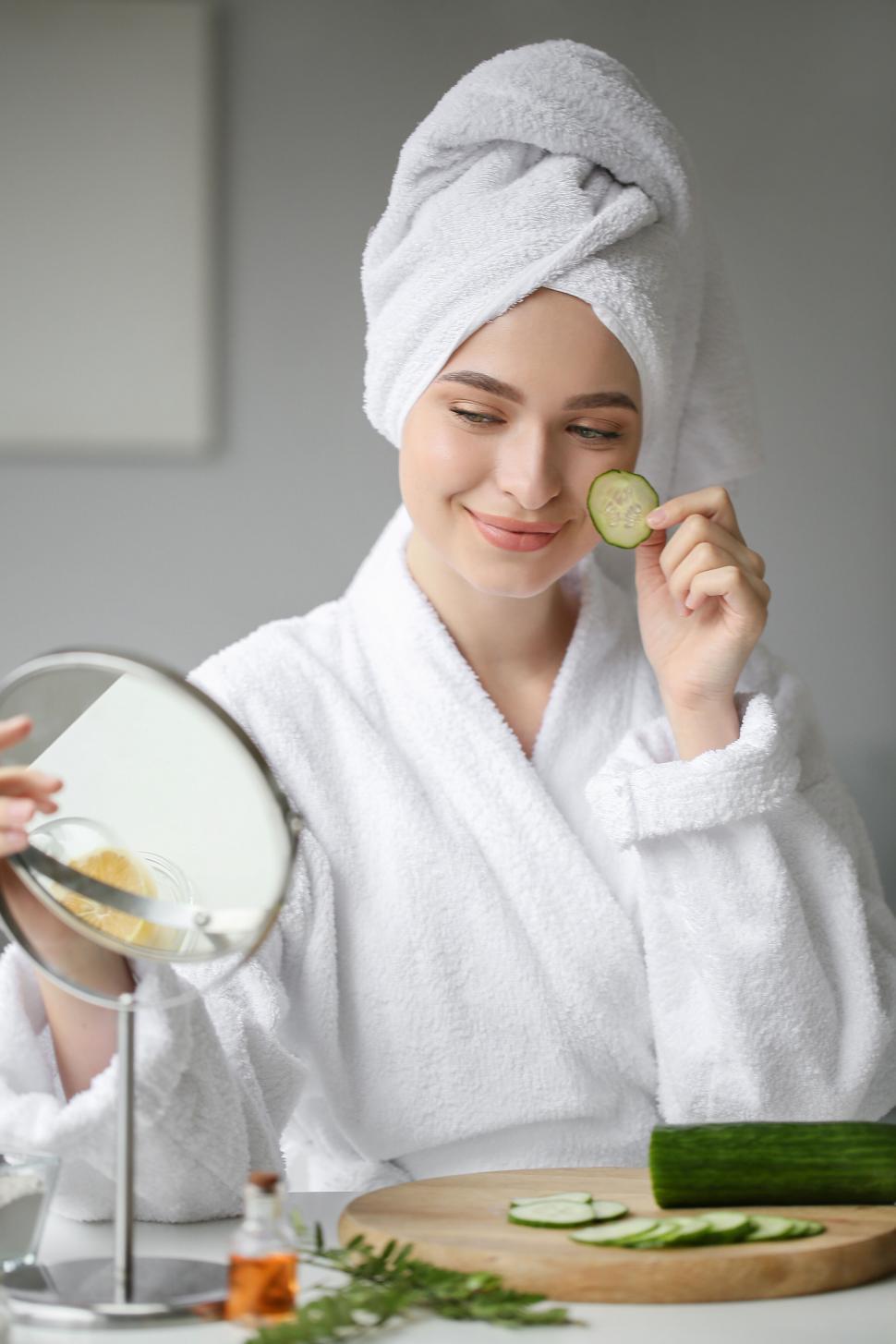 Free Image of A woman in a white robe holding a cucumber slice on her face 
