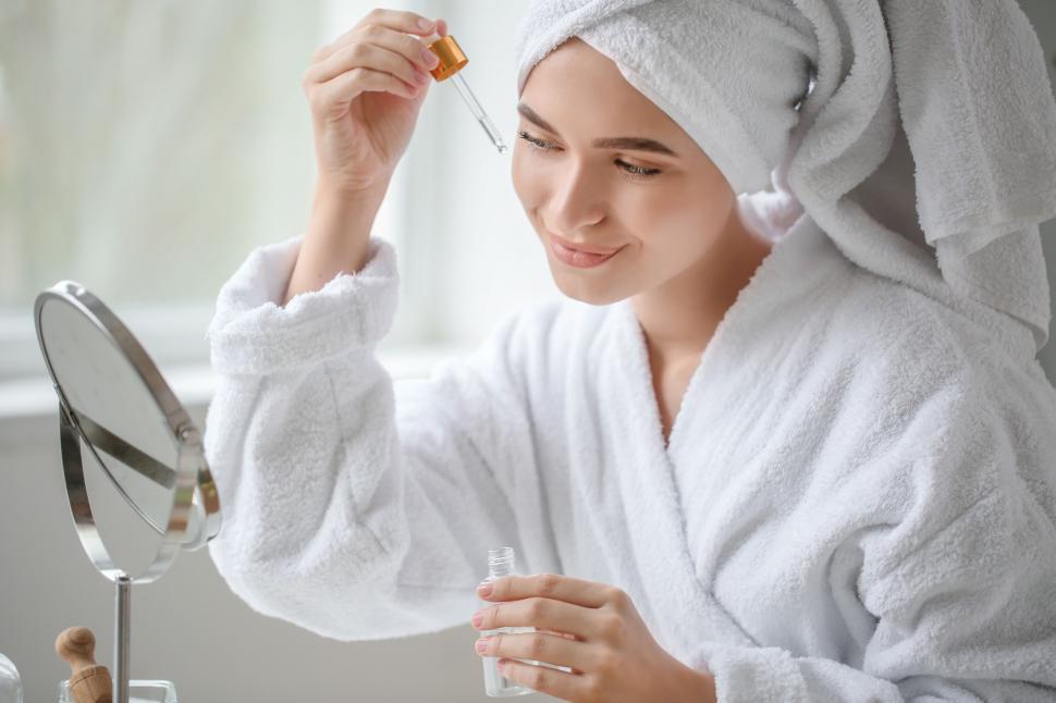 Free Image of A woman in a white robe holding a dropper and a bottle of oil 