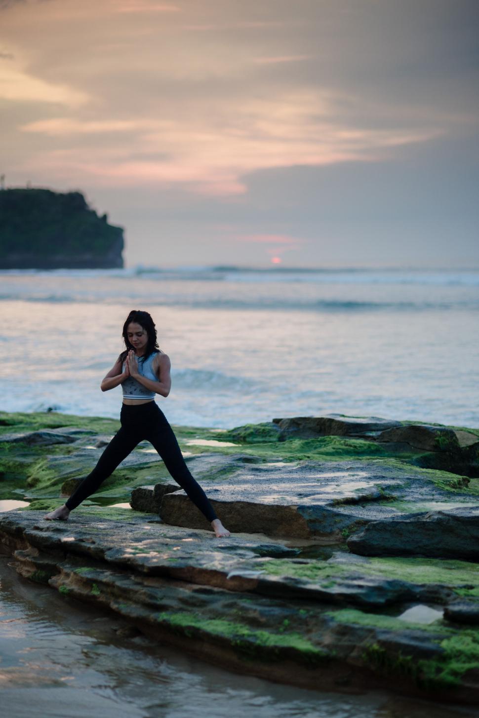 Free Image of A woman standing on a rock near water 