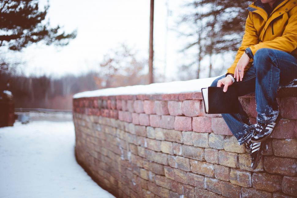 Free Image of Person sitting on brick wall holding a tablet 