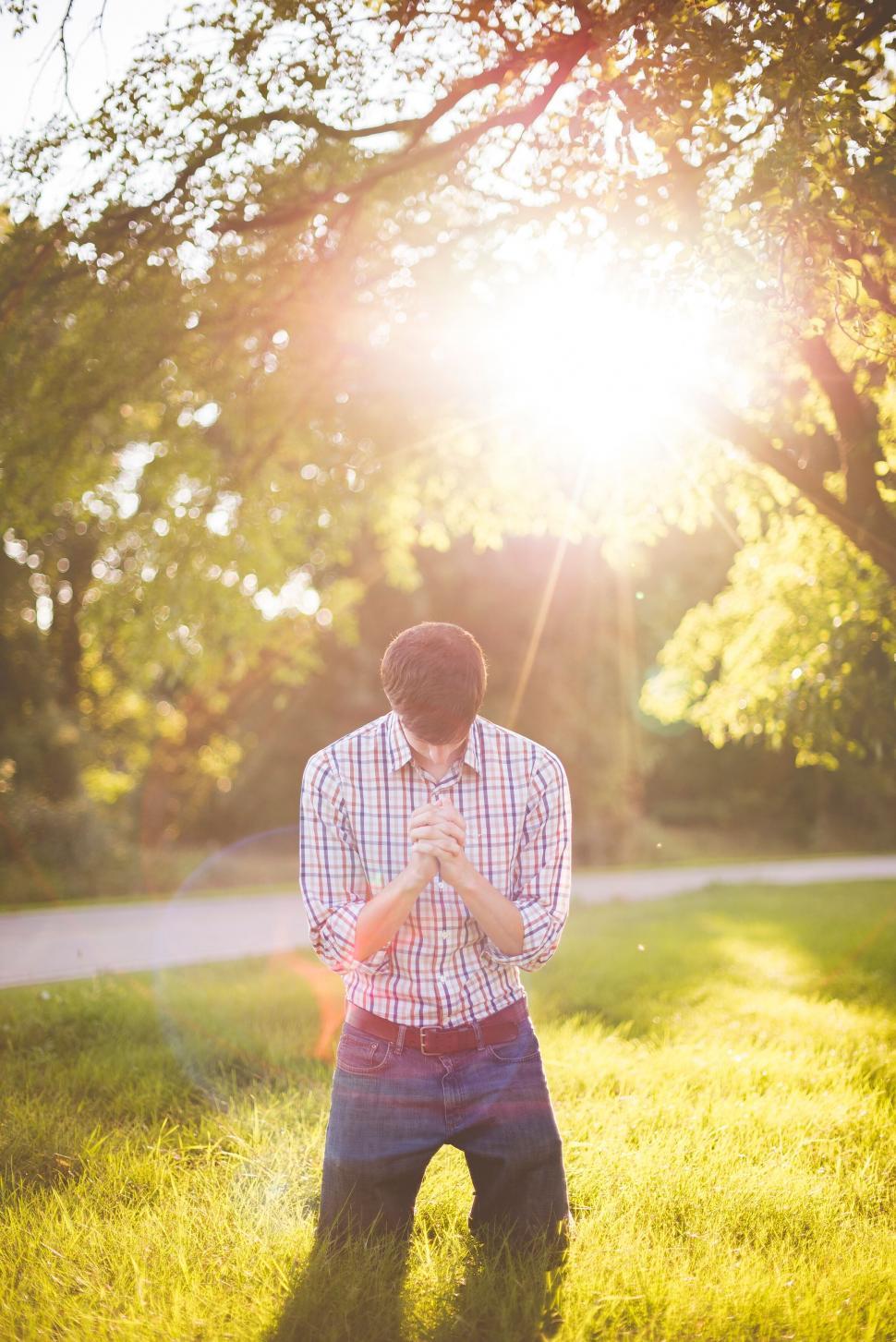 Free Image of Man praying in sunlit green park 