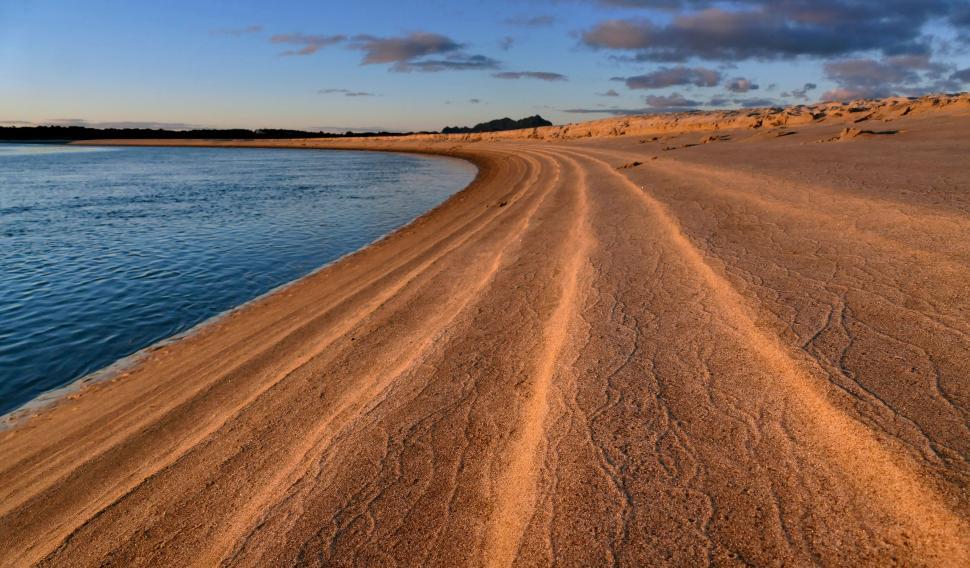 Free Image of Sunset casting golden light on a sandy beach 