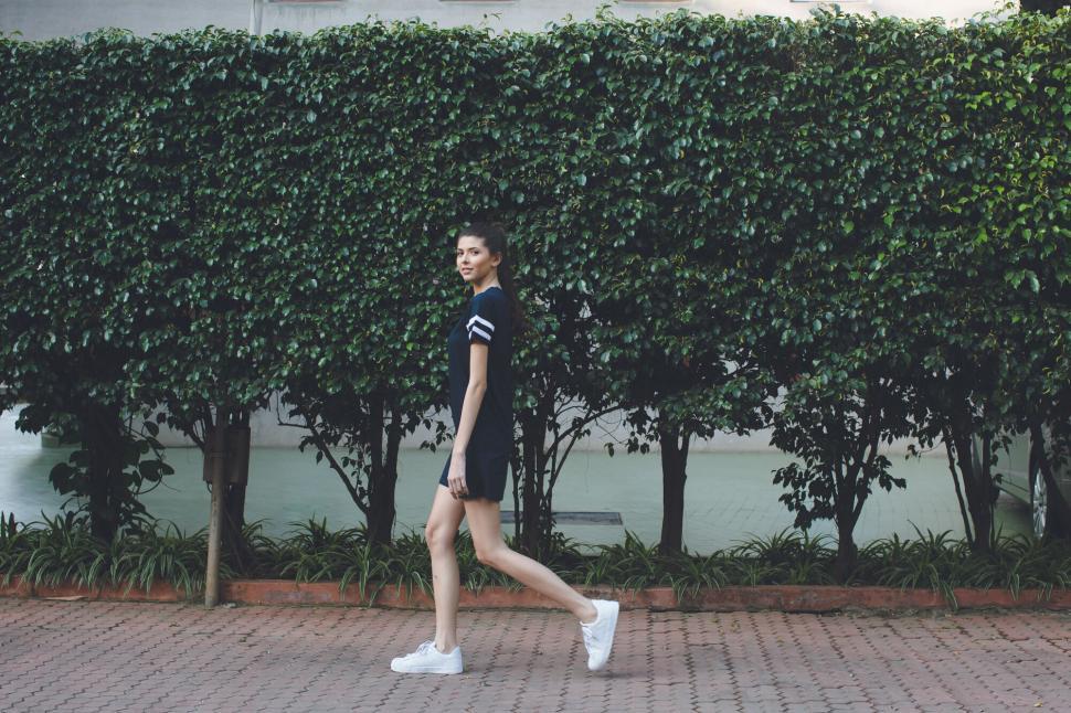 Free Image of Woman walking along a hedge backdrop 