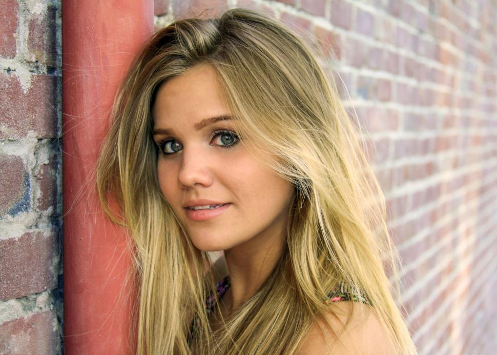 Free Image of Blonde girl smiling near brick wall 