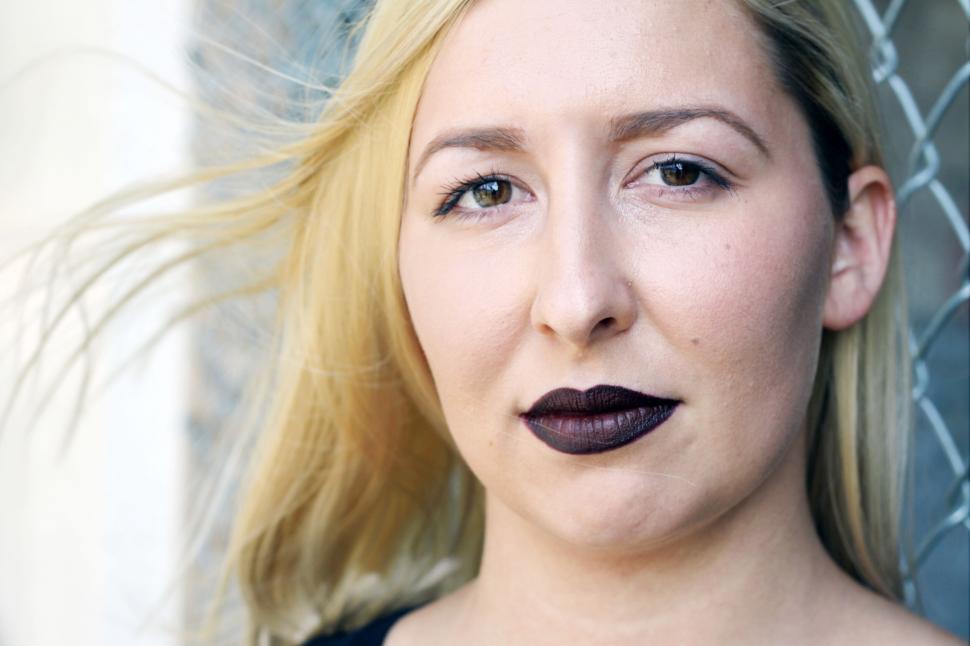 Free Image of Blonde woman with dark lipstick behind fence 