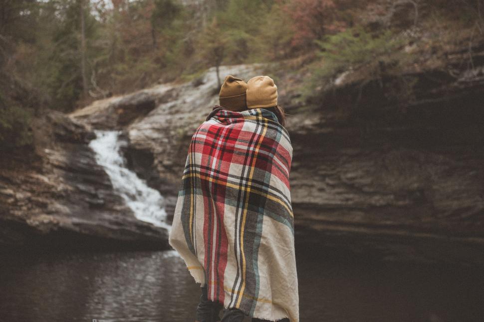 Free Image of Person wrapped in plaid blanket by waterfall 