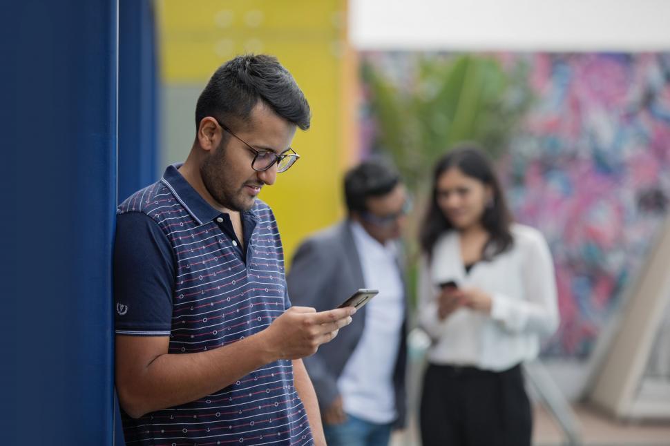 Free Image of Man reading phone outdoors with people 