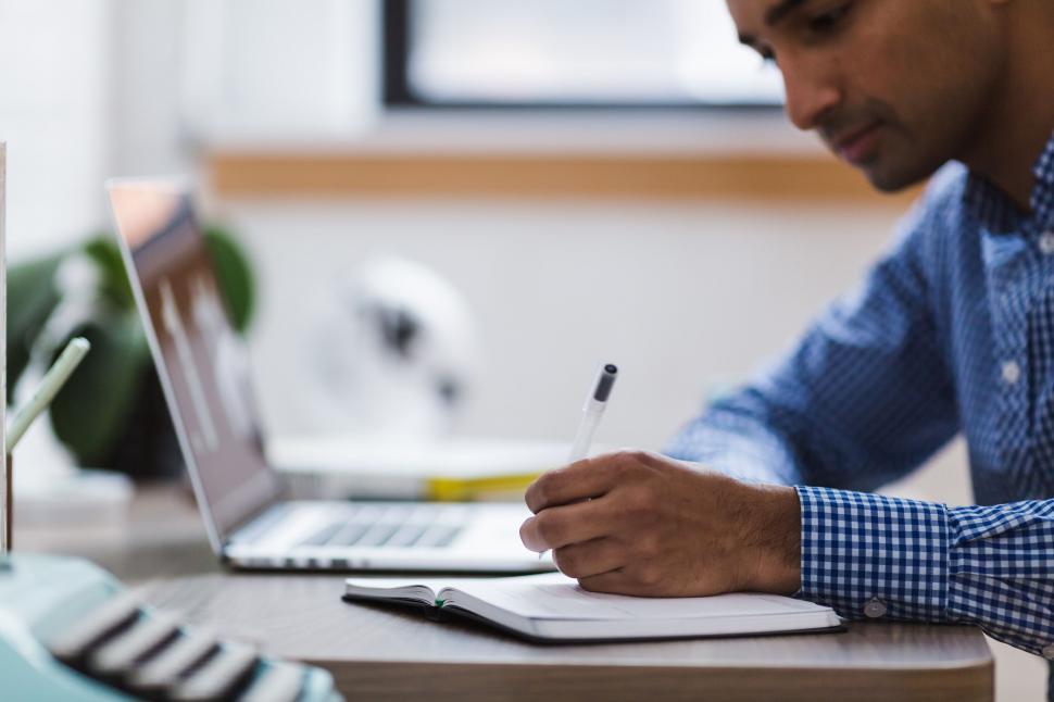 Free Image of Person writing notes beside laptop 