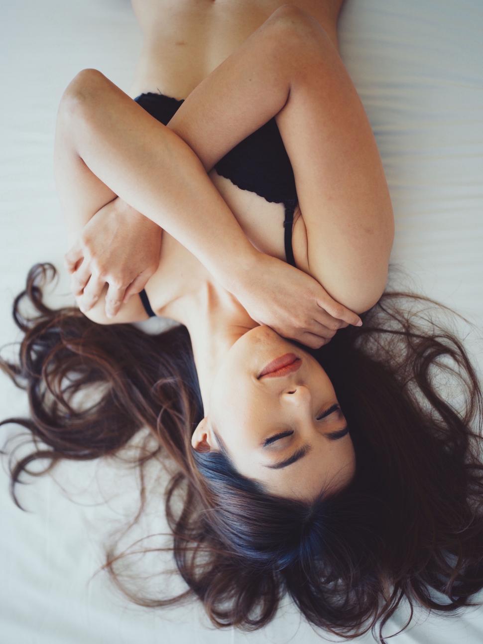 Free Image of Woman lying on bed covering herself with arms 