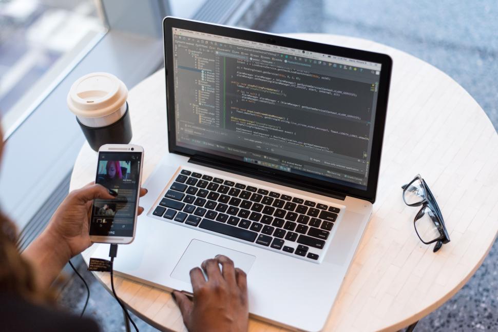 Free Image of Hands holding a smartphone and working on laptop 