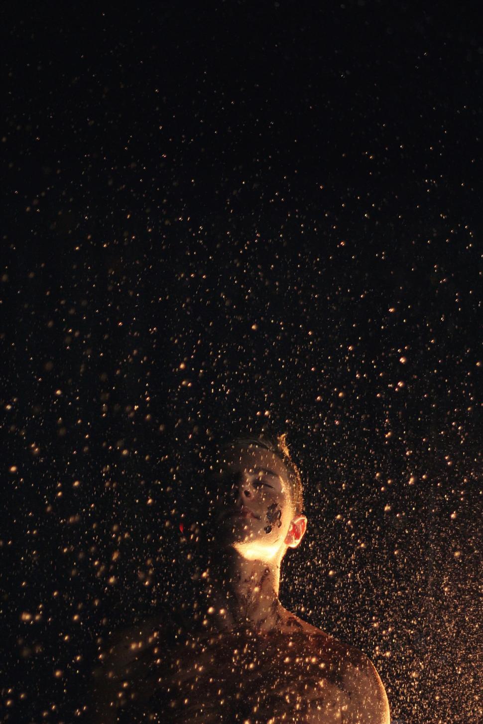 Free Image of Man surrounded by golden sparkles in darkness 