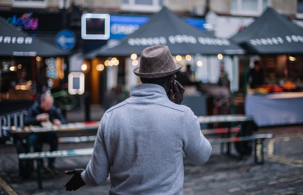 Free Image of Man in hat talking on phone at market street 