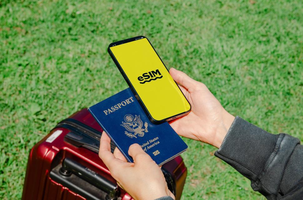 Free Image of A hand holding both a passport and a phone with an eSIM, indicating the modern necessities for international travel  