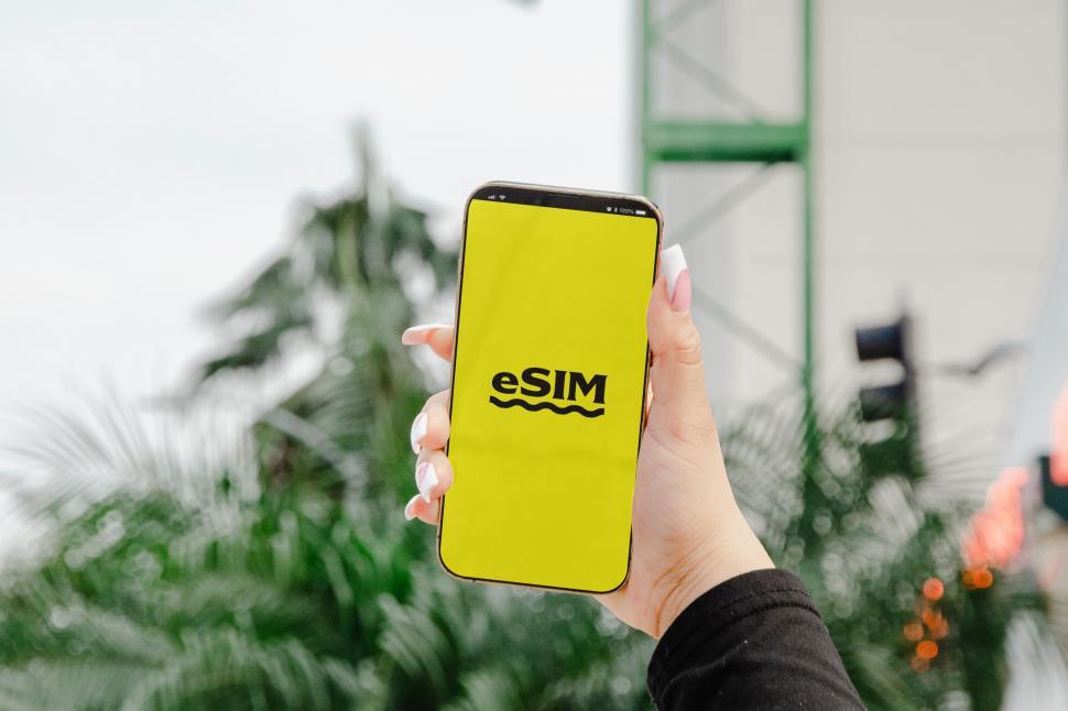 Free Image of A hand holding both a passport and a phone with an eSIM, indicating the modern necessities for international travel  