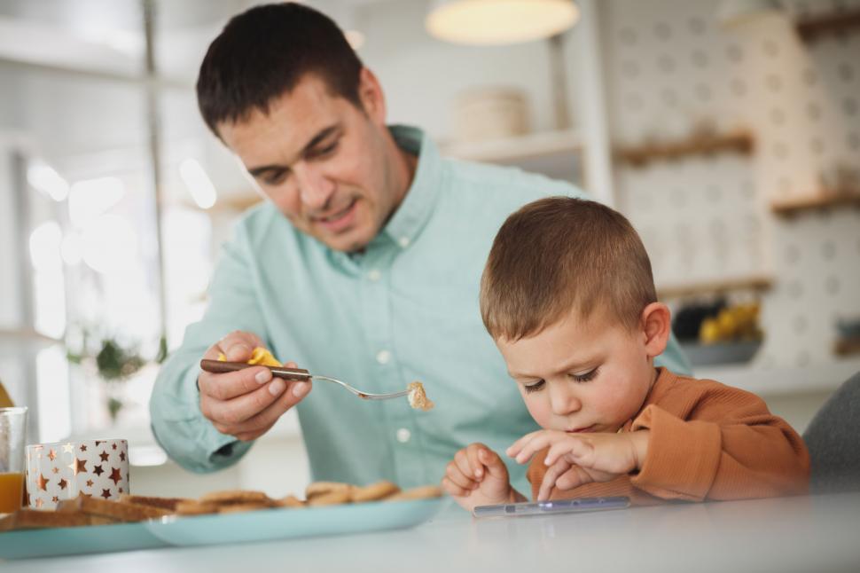 Free Image of Dad feeding his distracted son 