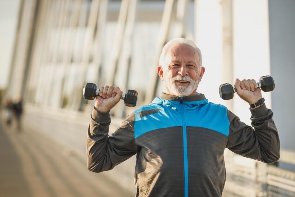 Free Image of Smiling senior man with weights on city bridge 