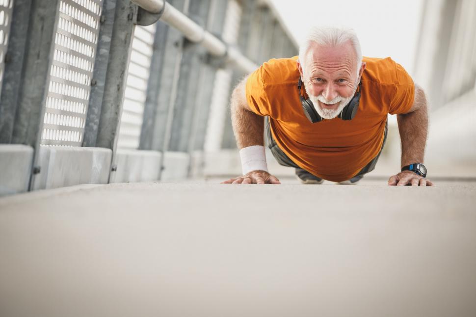 Free Image of Elderly man doing pushups on a sunny bridge 
