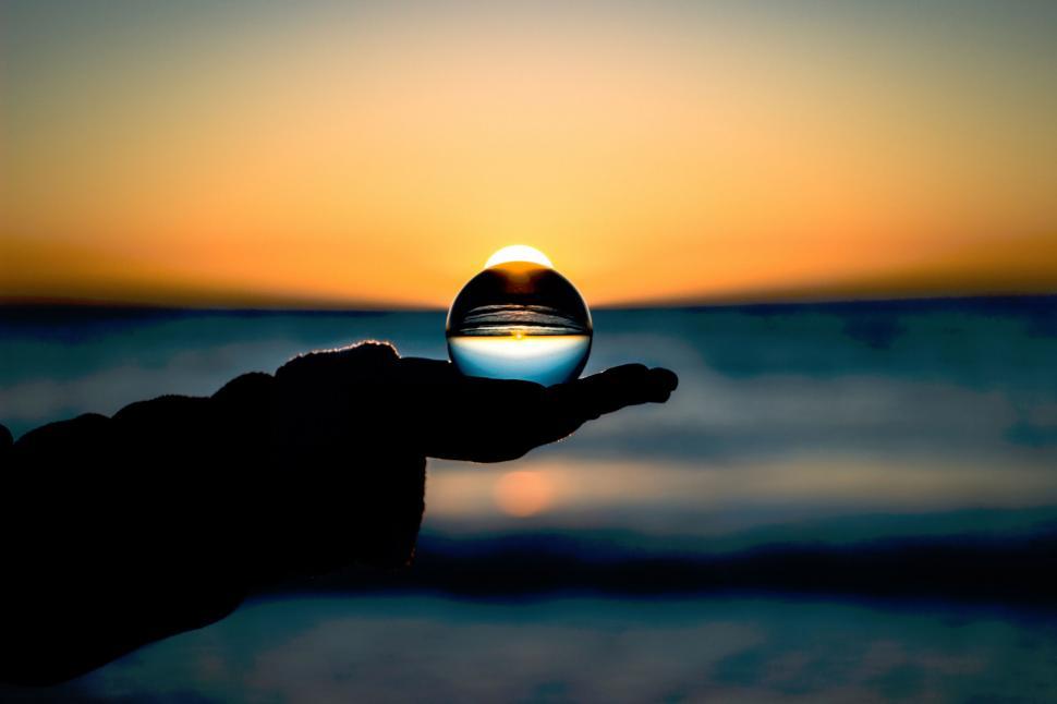 Free Image of Crystal ball reflecting a serene sunset over water 