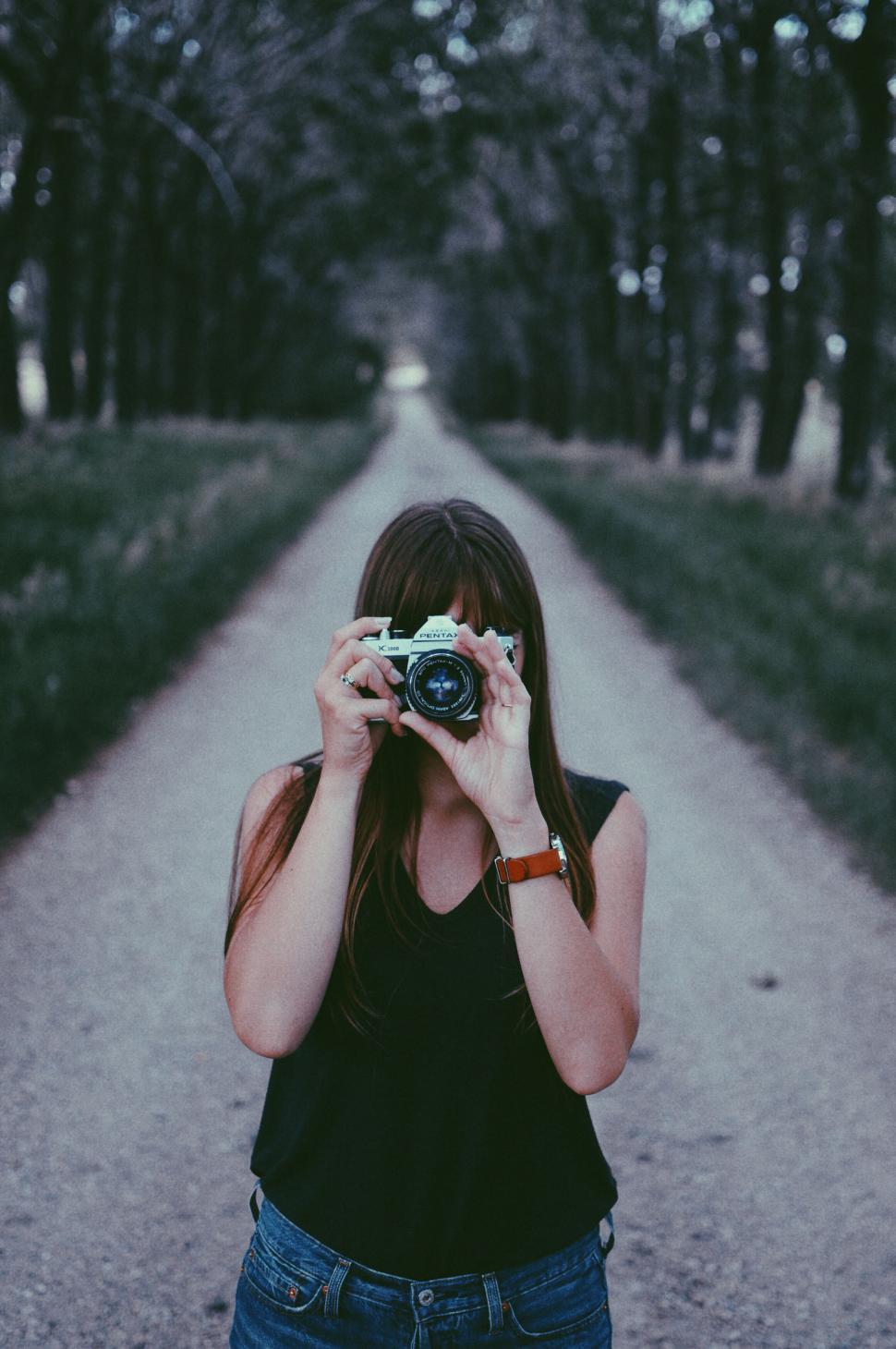 Free Image of Woman aiming camera at viewer down a path 