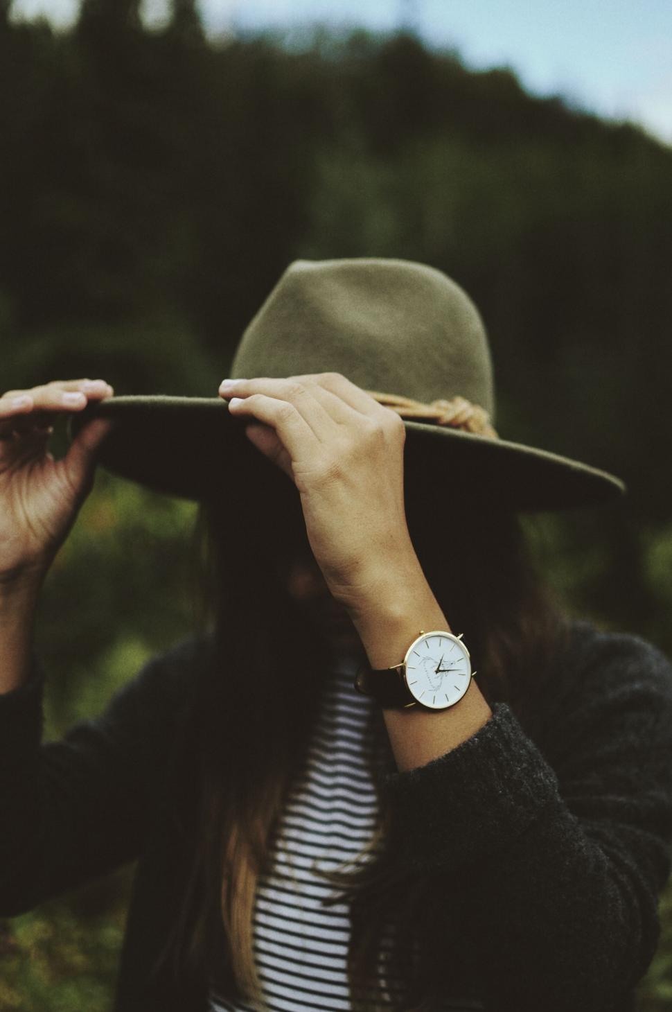 Free Image of Woman holding brim of hat in natural setting 